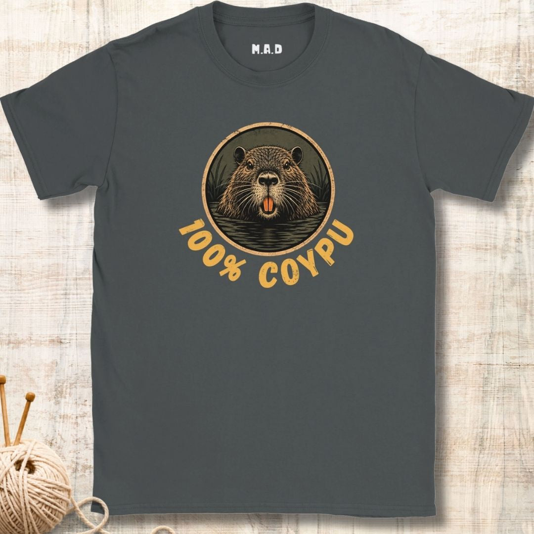 A dark gray t-shirt with a circular graphic of a coypu's face and the text '100% COYPU' in tan, displayed flat on a light wood background with a ball of yarn in the corner.