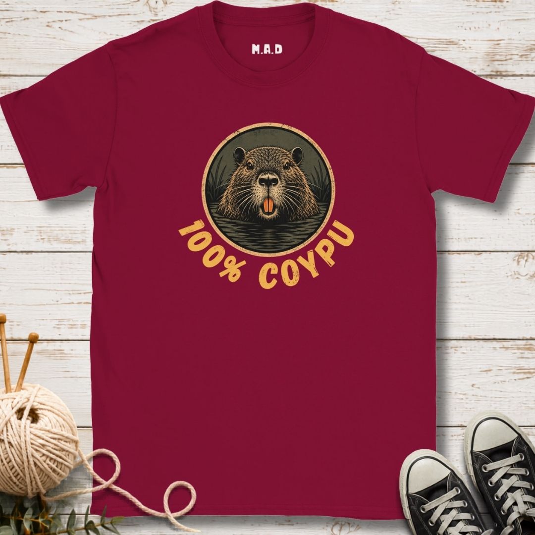 A maroon short-sleeve t-shirt laid flat on a white wood plank background, featuring a circular graphic of a coypu's face with the text '100% COYPU' in yellow. 