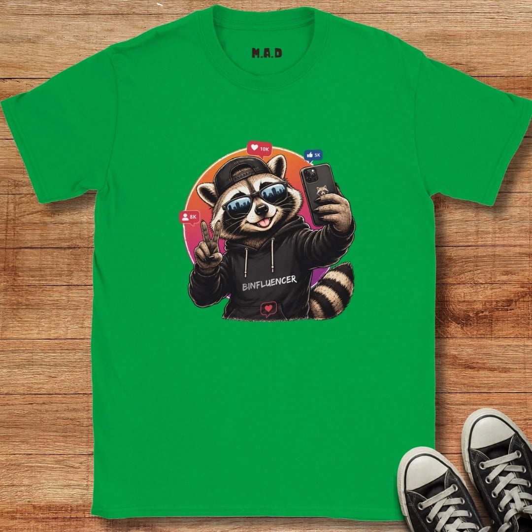 Green t-shirt with a raccoon graphic holding a phone on a wooden surface