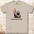 Beige t-shirt with a sloth holding a foam finger and text 'Doing Nothing Well' on a wooden surface.