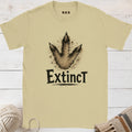 Beige t-shirt with dinosaur footprint graphic and 'Extinct' text on a wooden surface.