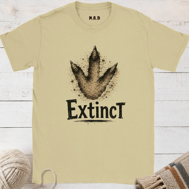 Beige t-shirt with dinosaur footprint graphic and 'Extinct' text on a wooden surface.