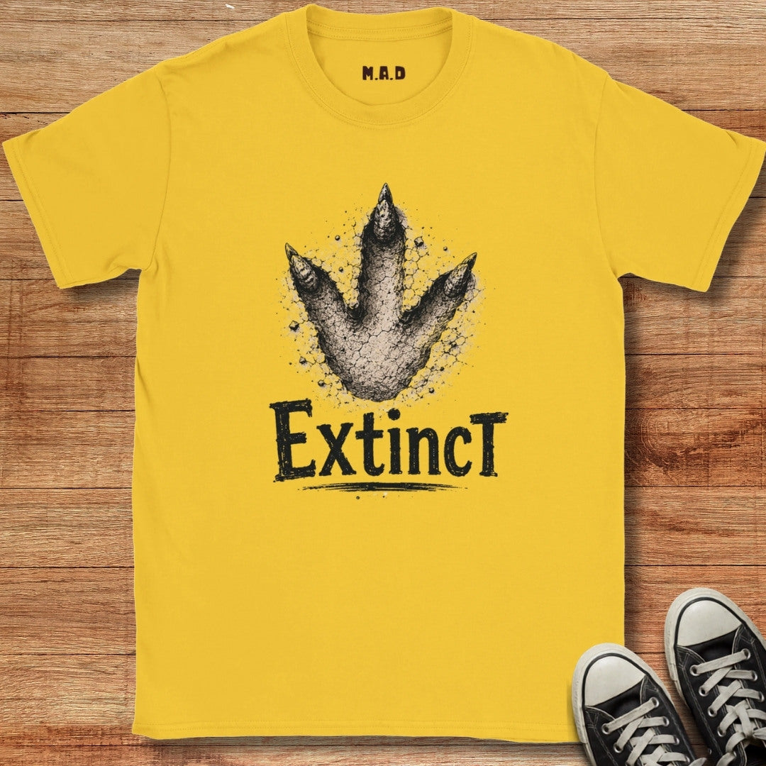 Yellow t-shirt with dinosaur footprint graphic and 'Extinct' text on a wooden surface
