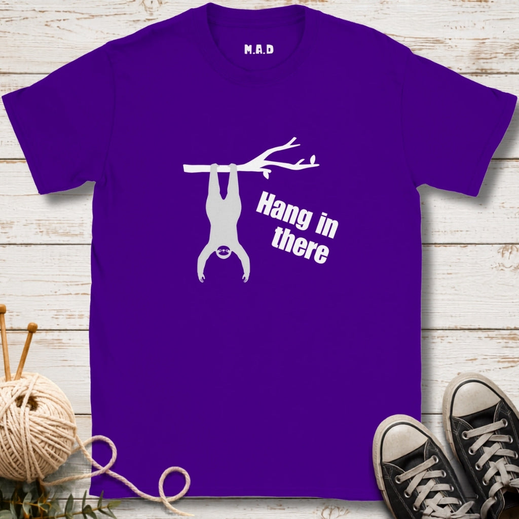 Purple t-shirt with 'Hang in there' graphic on a wooden surface with sneakers and yarn.
