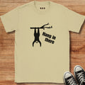 Beige t-shirt with a sloth graphic and 'Hang in there' text on a wooden surface, next to black sneakers.