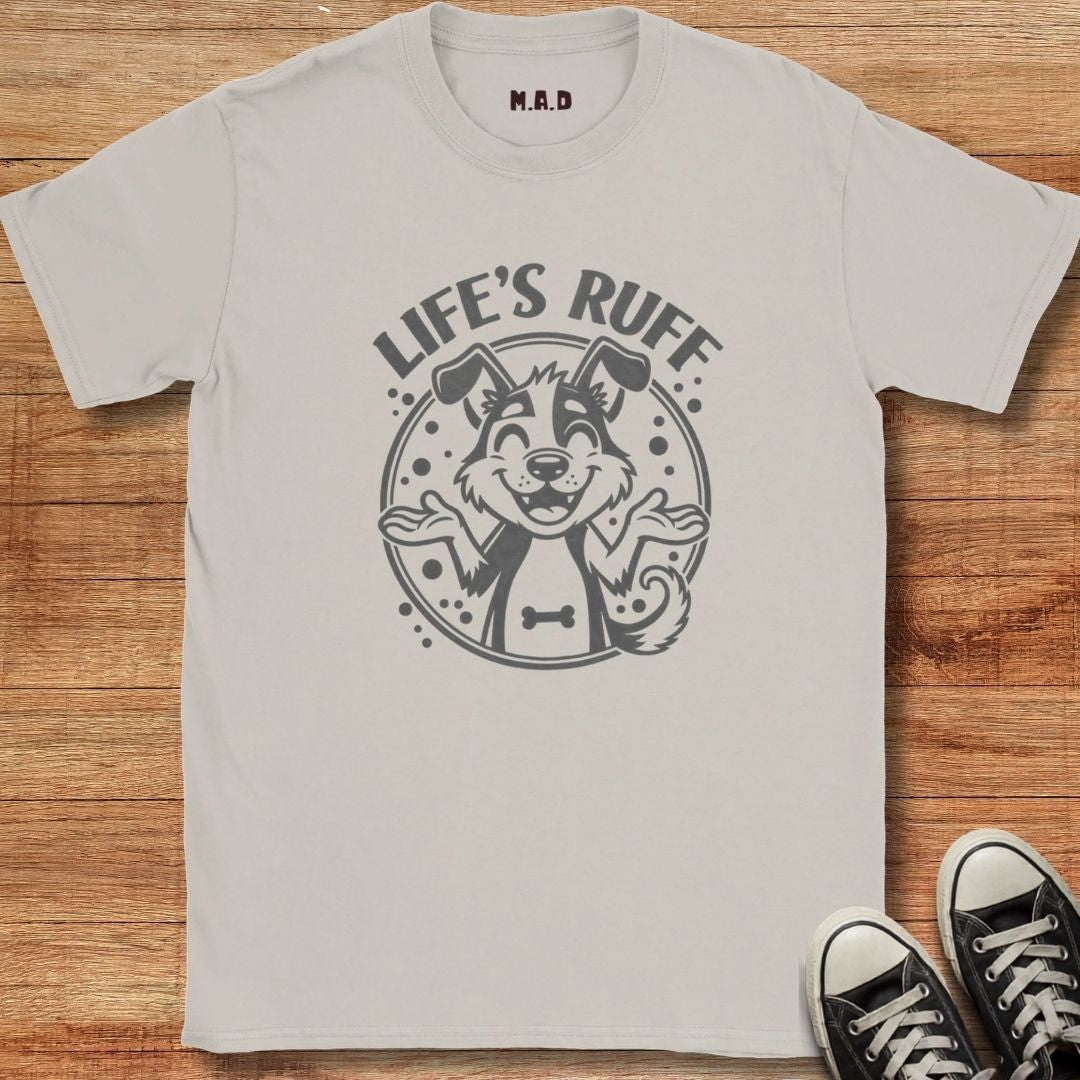 A light gray crewneck t-shirt with a dark gray graphic of a dog wearing sunglasses and the text 'LIFE'S RUFF' on the front, laid flat on a wooden surface with black sneakers partially visible in the corner.