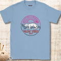 A light blue crewneck t-shirt with a retro-style graphic of a sleeping white cat under a pink and blue sunset, with the text 'MEOW VIBES ONLY' in red. The shirt is laid flat on a light wood background with a ball of yarn and knitting needles visible in the corner.