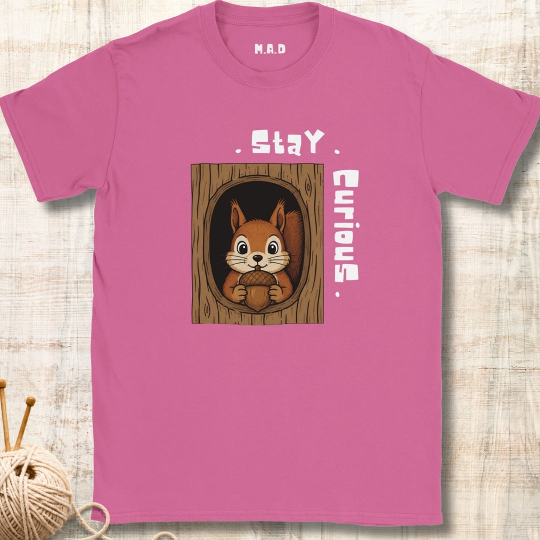 A pink short-sleeve t-shirt with a graphic of a curious squirrel in a tree hole, featuring the text 'Stay Curious' 