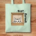Tote bag with a cat illustration and 'Stay Curious' text on a wooden surface
