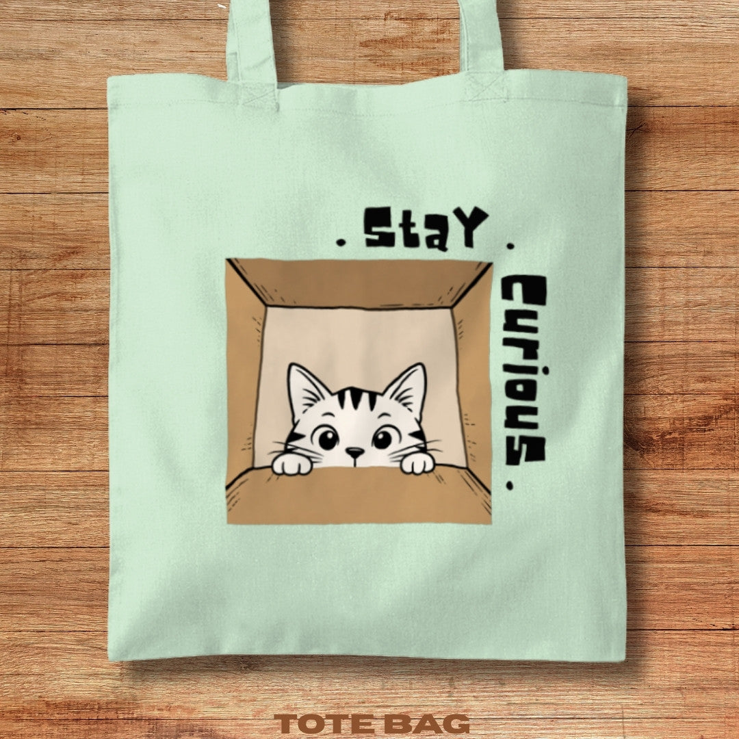 Tote bag with a cat illustration and 'Stay Curious' text on a wooden surface