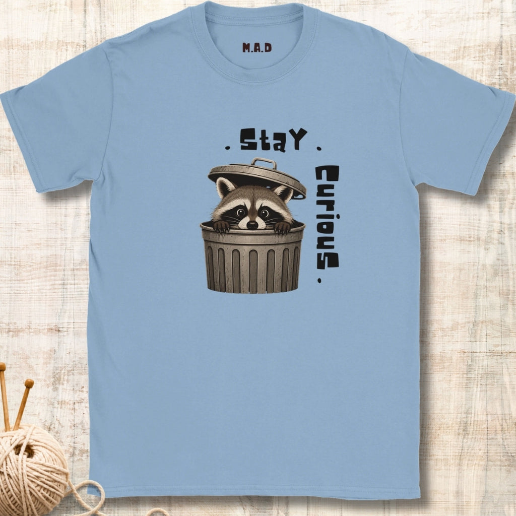 A light blue crewneck t-shirt featuring a graphic of a raccoon peeking out of a trash can with the text '. Stay.