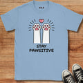 Light blue t-shirt with cartoon paw design and text 'Stay Pawsitive' on a wooden surface.