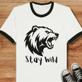 White t-shirt with black bear graphic and 'Stay Wild' text on a wooden surface