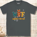 A dark gray crewneck t-shirt featuring a graphic design of a fox and the text 'WTF WHERE'S THE FOX' in a distressed, retro style. The t-shirt is displayed flat on a light wood background with a ball of yarn and knitting needles in the bottom-left corner.
