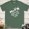 A sage green t-shirt with a white graphic of safari animals and the text 'WALK ON THE WILD SIDE' laid flat on a white wood background with knitting yarn and black sneakers as props.