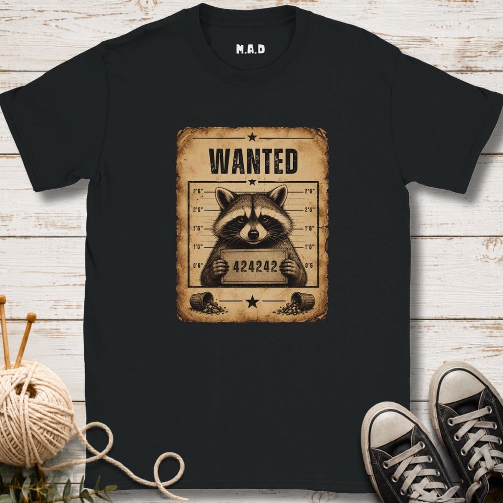 Black t-shirt with a raccoon wanted poster design on a wooden surface.